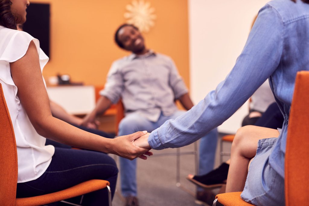 Multicultural men and woman joining hands in therapy.