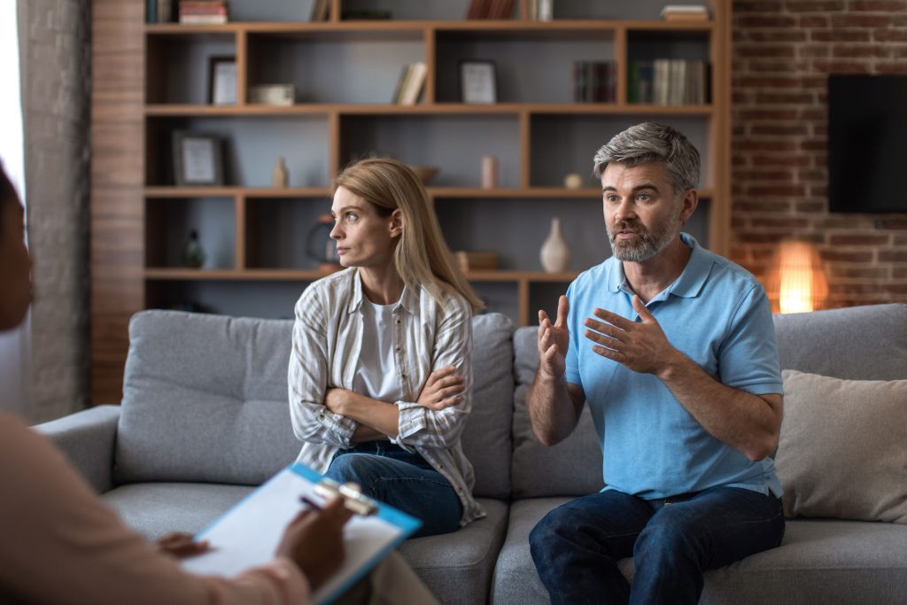 Man explaining to the therapist while his wife looks disappointed.