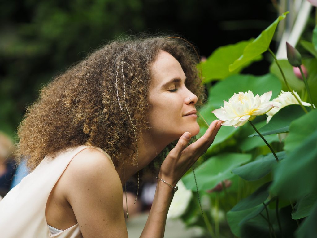 Woman with curly hair closed eyes smelling flowers.