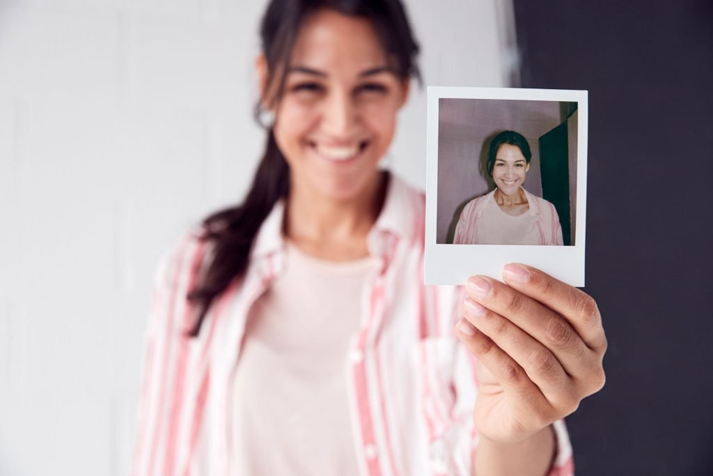 Woman smiling while holding a photo of her.