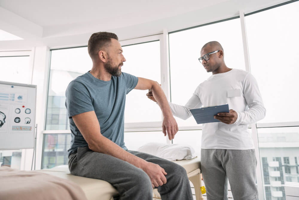 male specialist evaluating a patient's elbow mobility during a physical rehabilitation and yoga therapy session